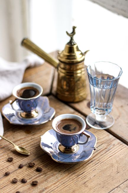 Blue porcelain cups with coffee, golden pot, and glass on a wooden table.