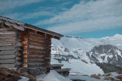 Free A cozy wooden cabin amidst snow-covered mountains under a blue sky. Stock Photo