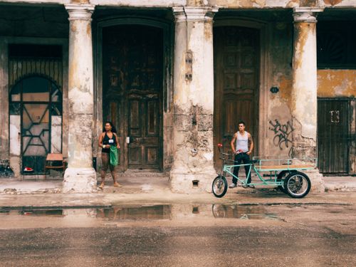 Free Man and woman in front of historic building in Havana, Cuba with bicycle cart. Stock Photo