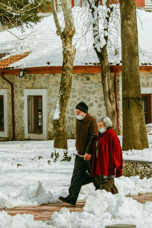 Free Elderly couple holding hands and wearing masks, walking through a snowy landscape in winter. Stock Photo