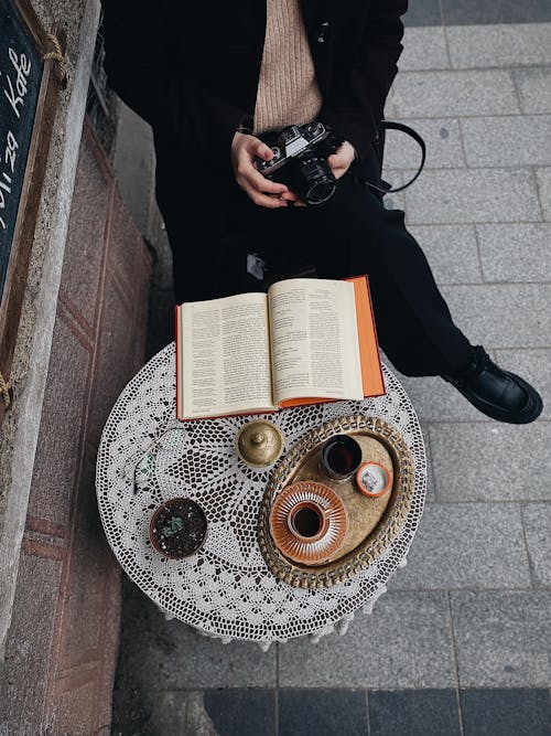 açık kitap, bacaklar geçti, bir fincan kahve içeren Ücretsiz stok fotoğraf