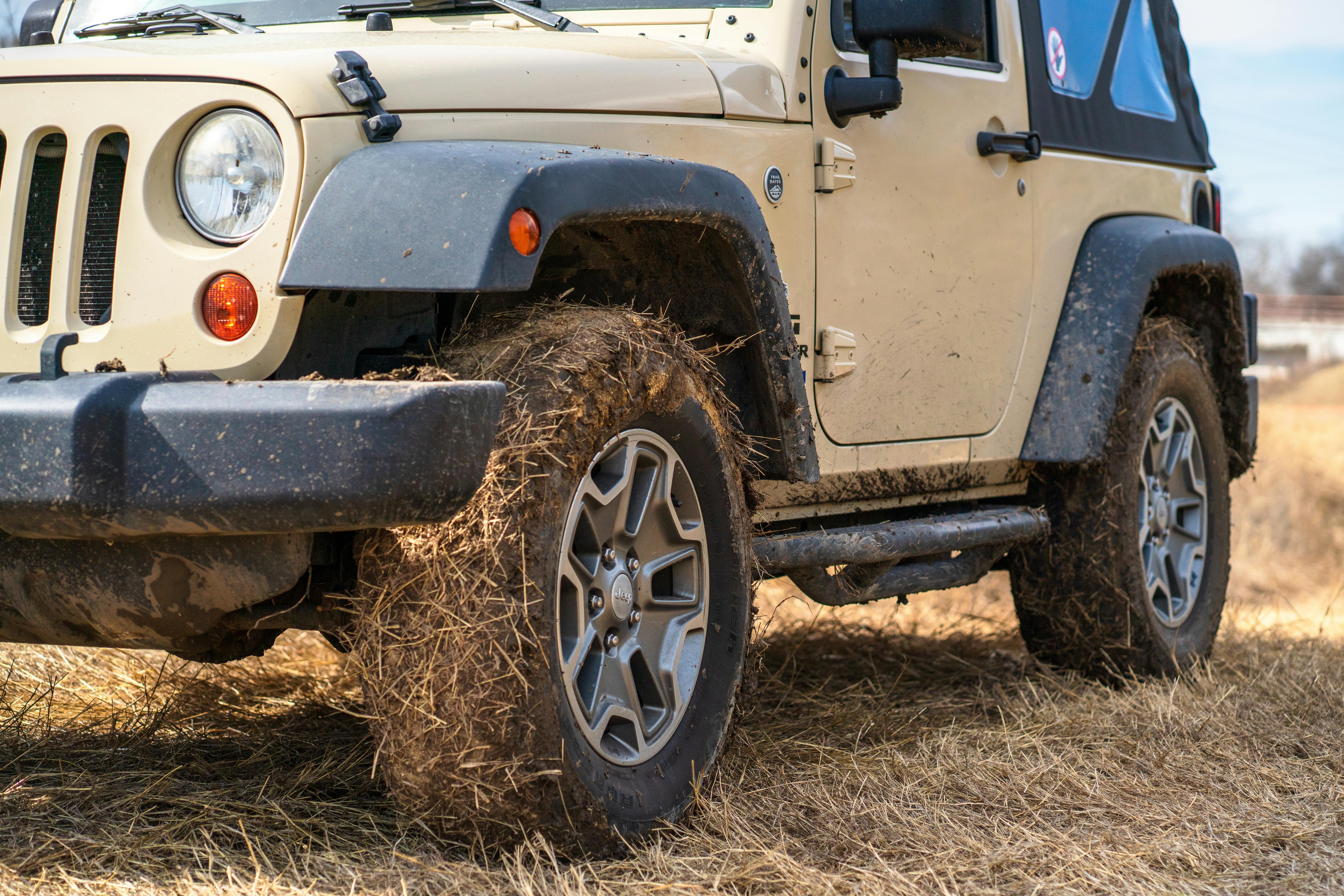 Close-up of an off-road vehicle parked in a dry grass field with muddy tires.