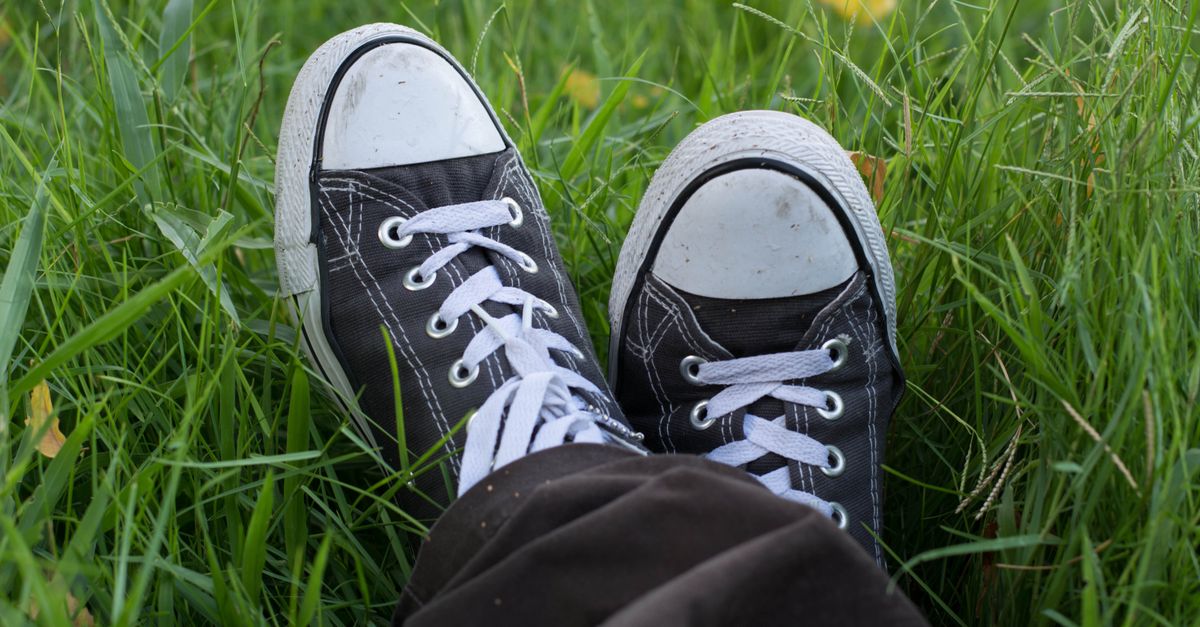 Close-up of classic black sneakers on vibrant grass, capturing a relaxed outdoor moment.