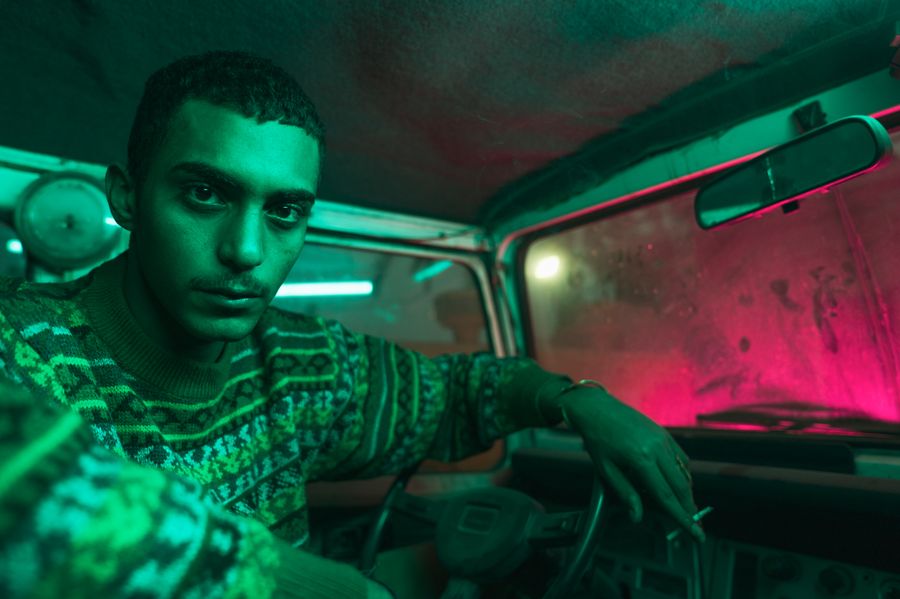 A young man in a car interior lit by green and pink neon. Photo by zaid mohammed on Pexels