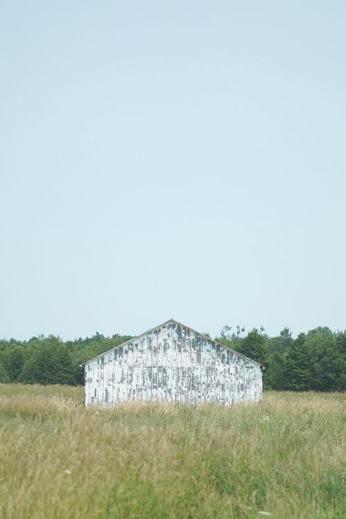Free An abandoned barn amidst a grassy field under a bright clear sky in the countryside. Stock Photo