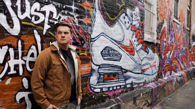 Man leaning against a graffiti-covered brick wall featuring a colorful mural.