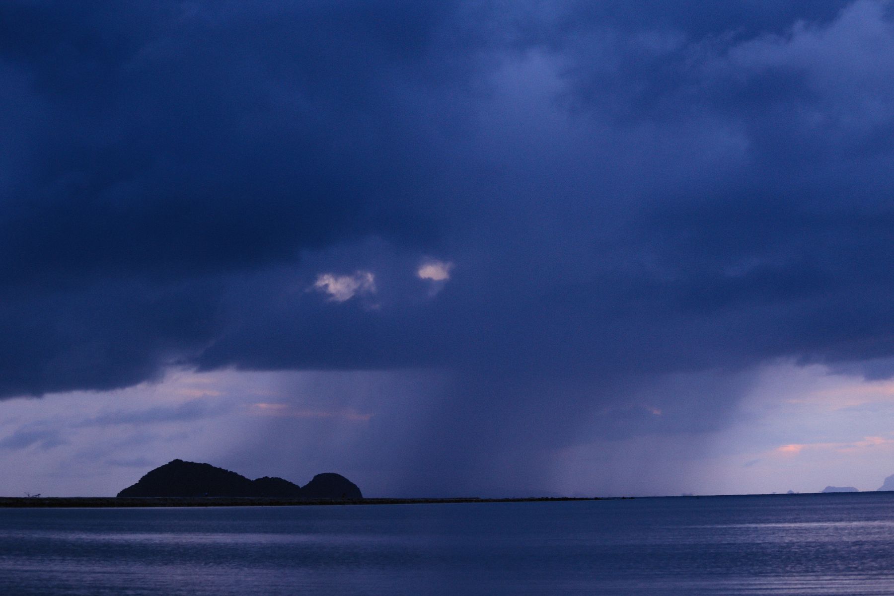 Silhouetted island under dark rain clouds at twilight — Alexey Demidov on Pexels