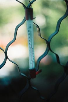 A close-up of an outdoor thermometer against a blurred green background.