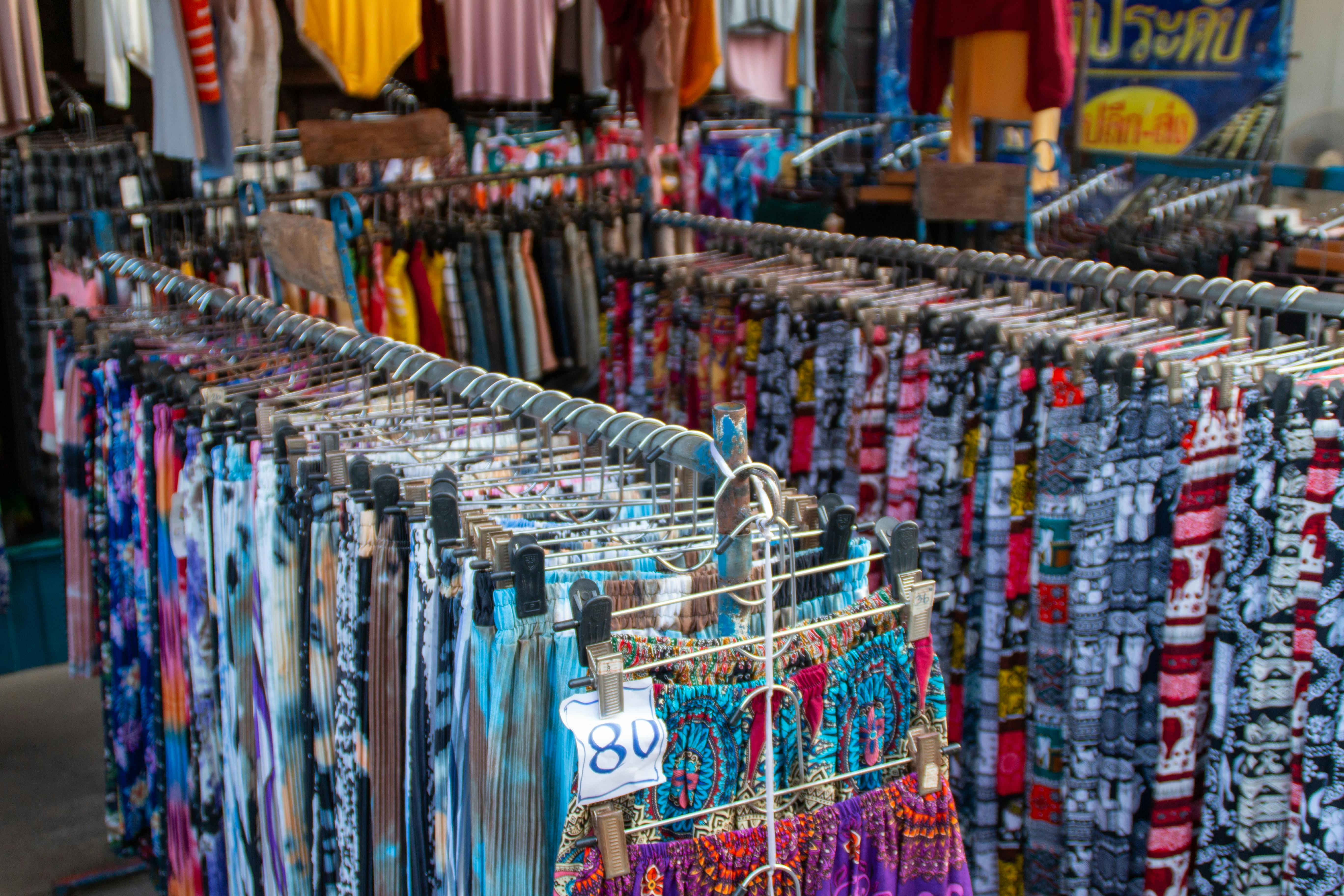 Vibrant array of clothing on racks in an outdoor market setting.