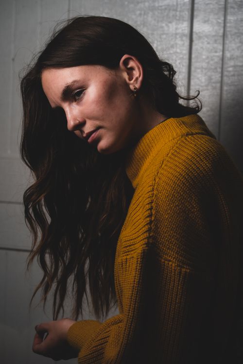 Free A thoughtful woman in a yellow sweater poses against a textured wall. Moody and artistic composition. Stock Photo