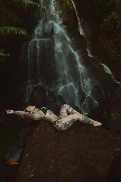 Free A tattooed woman lies on a rock near a waterfall, embracing nature's beauty. Stock Photo