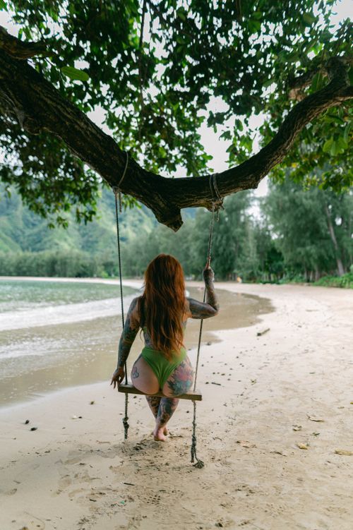 Free A tattooed woman sits on a swing by the ocean, embracing tranquility on a sandy beach. Stock Photo