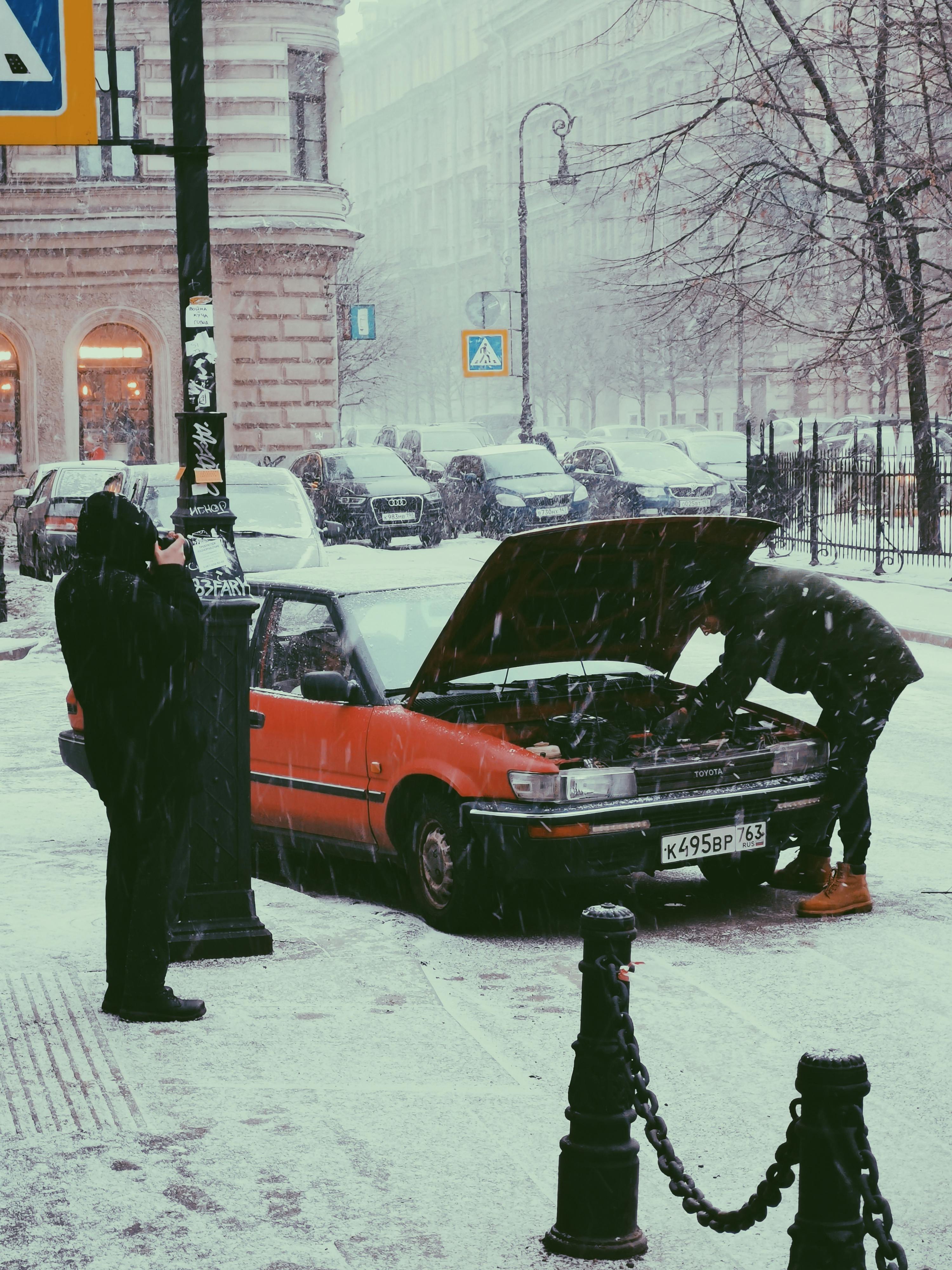 a person repairing a broken car under the snow
