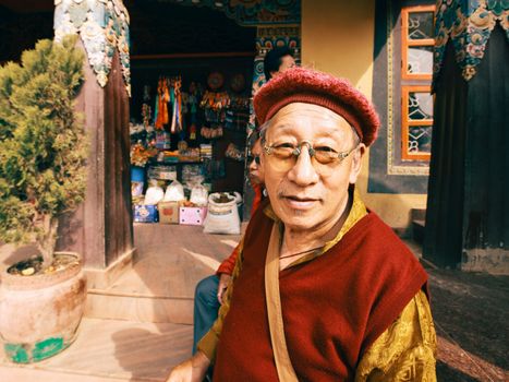 Portrait of an elderly man in traditional clothing outside a colorful shop on a sunny day.