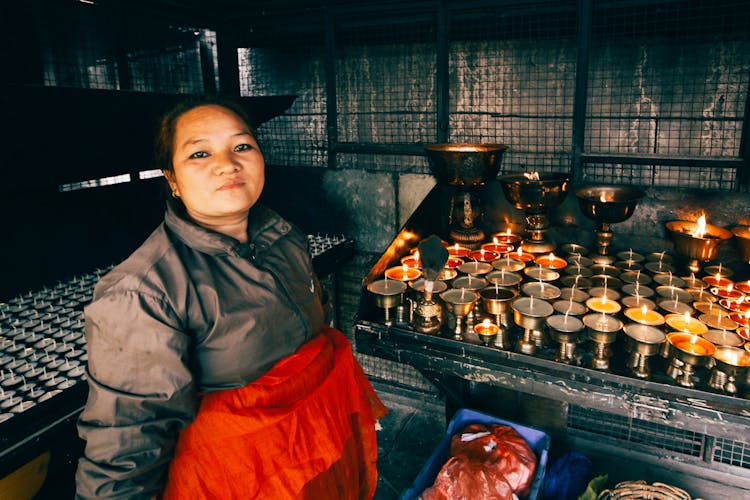 A Woman Standing Beside Prayer Candles On Rack