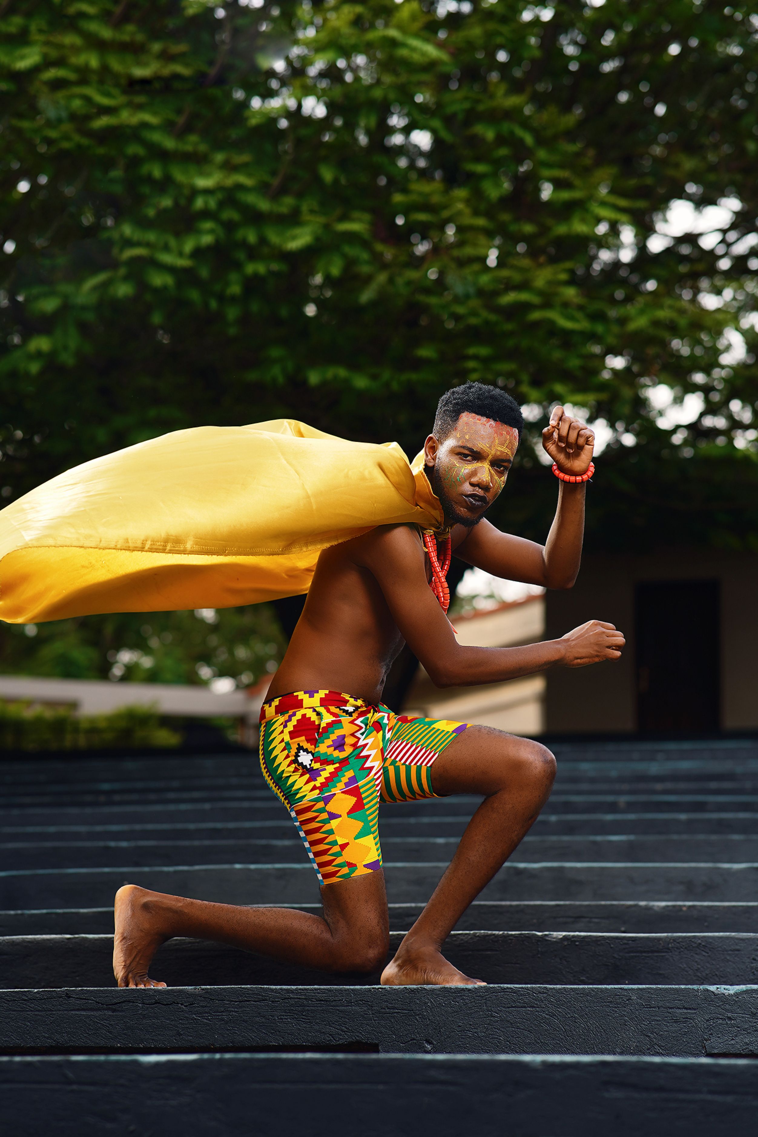 A man in vibrant traditional African clothing poses with pride outdoors.