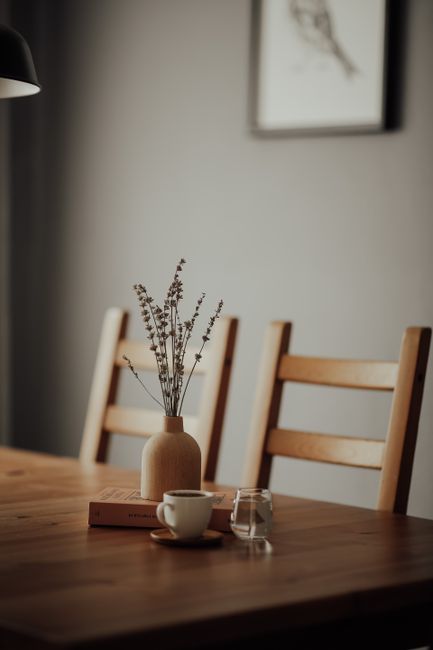 A minimalist dining setup with wooden furniture and a vase with branches, perfect for cozy interiors.