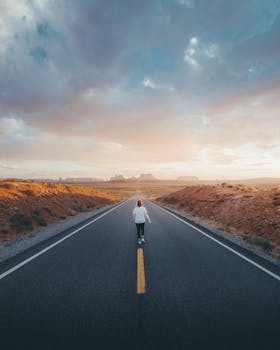 Person walking on a lonely highway in Arizona under a dramatic sky during sunset.
