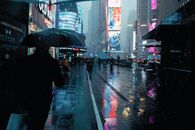 Pedestrians walking under umbrellas on a rainy night in Times Square, NYC.