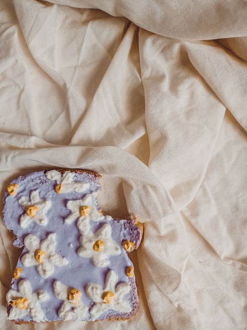 Free Artistic slice of bread with purple spread and decorative toppings on fabric background. Stock Photo