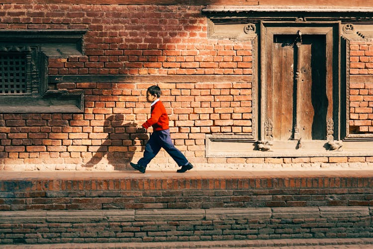 Boy In His Red Jacket Walking On The Sidewalk