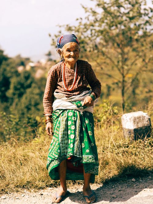 Free Portrait of an elderly woman wearing traditional attire, standing outdoors in a rural setting. Stock Photo