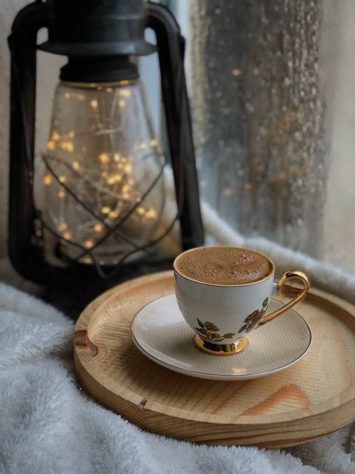 Free Warm coffee next to a glowing lantern and window, creating a cozy ambiance. Stock Photo
