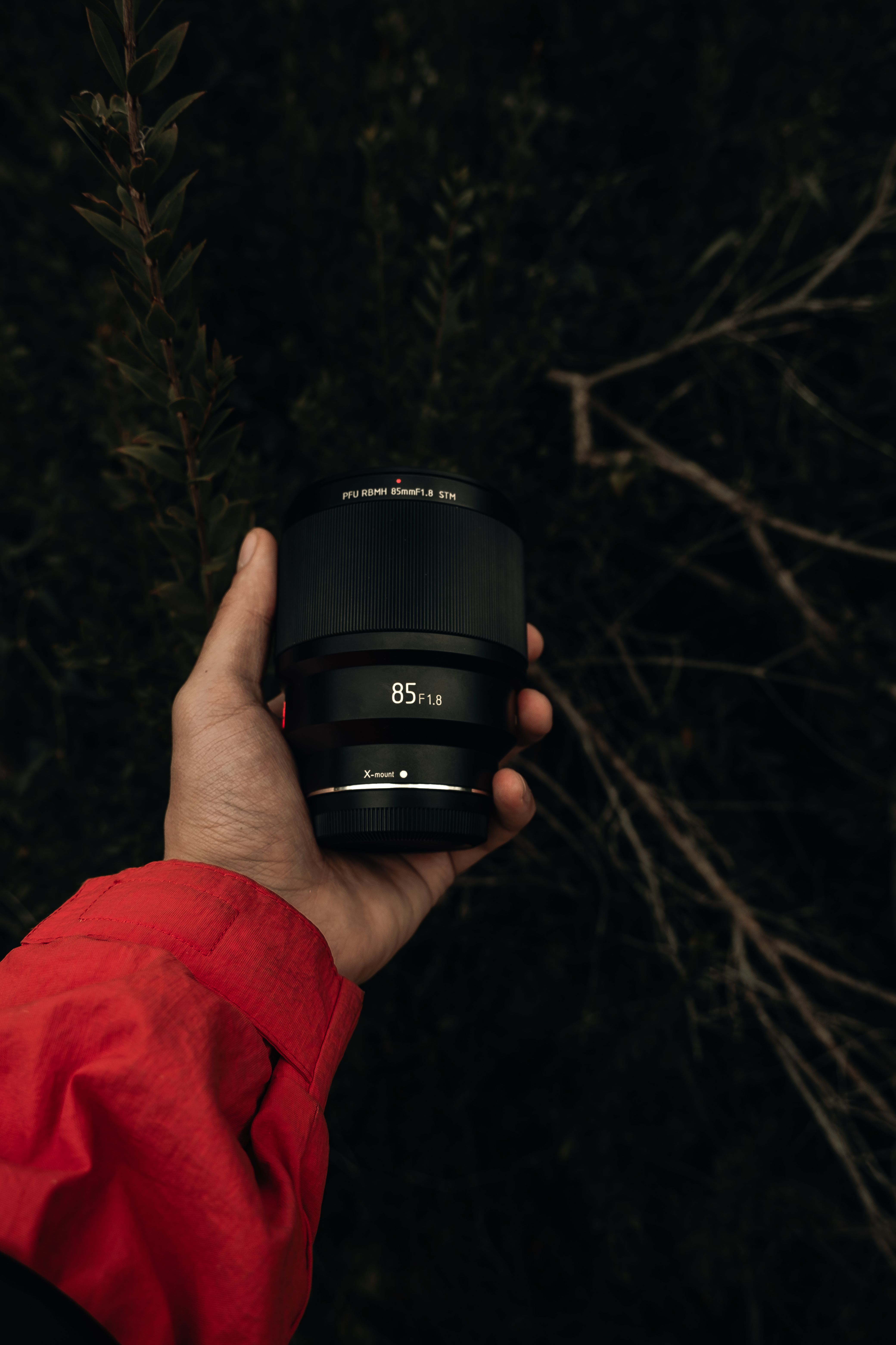 Detailed view of a hand holding an 85mm camera lens against a natural backdrop.