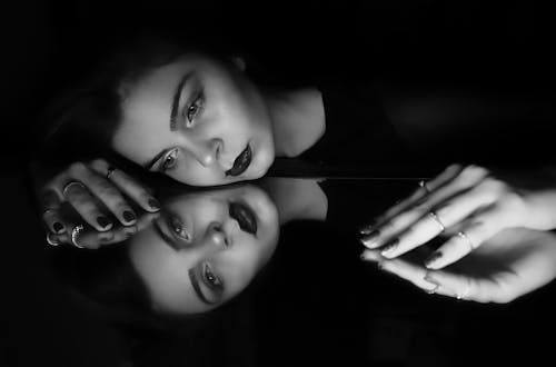 Grayscale Photo of Woman Leaning Head on Mirror 