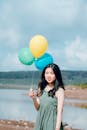 一名年轻女子在湖边举着彩色气球，享受阳光明媚的一天