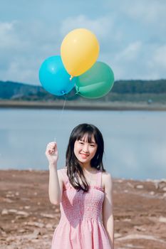 一位年轻女子手持五颜六色的气球，在风景秀丽的湖边散发着欢乐和休闲的气息