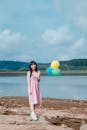 夏日阳光明媚，一位快乐的年轻女子拿着气球，站在宁静的湖边