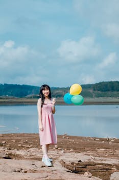 夏日阳光明媚，一位快乐的年轻女子拿着气球，站在宁静的湖边