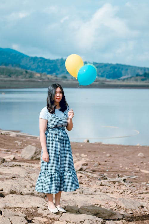Woman in White and Black Dress Stands While Holding Party Balloons