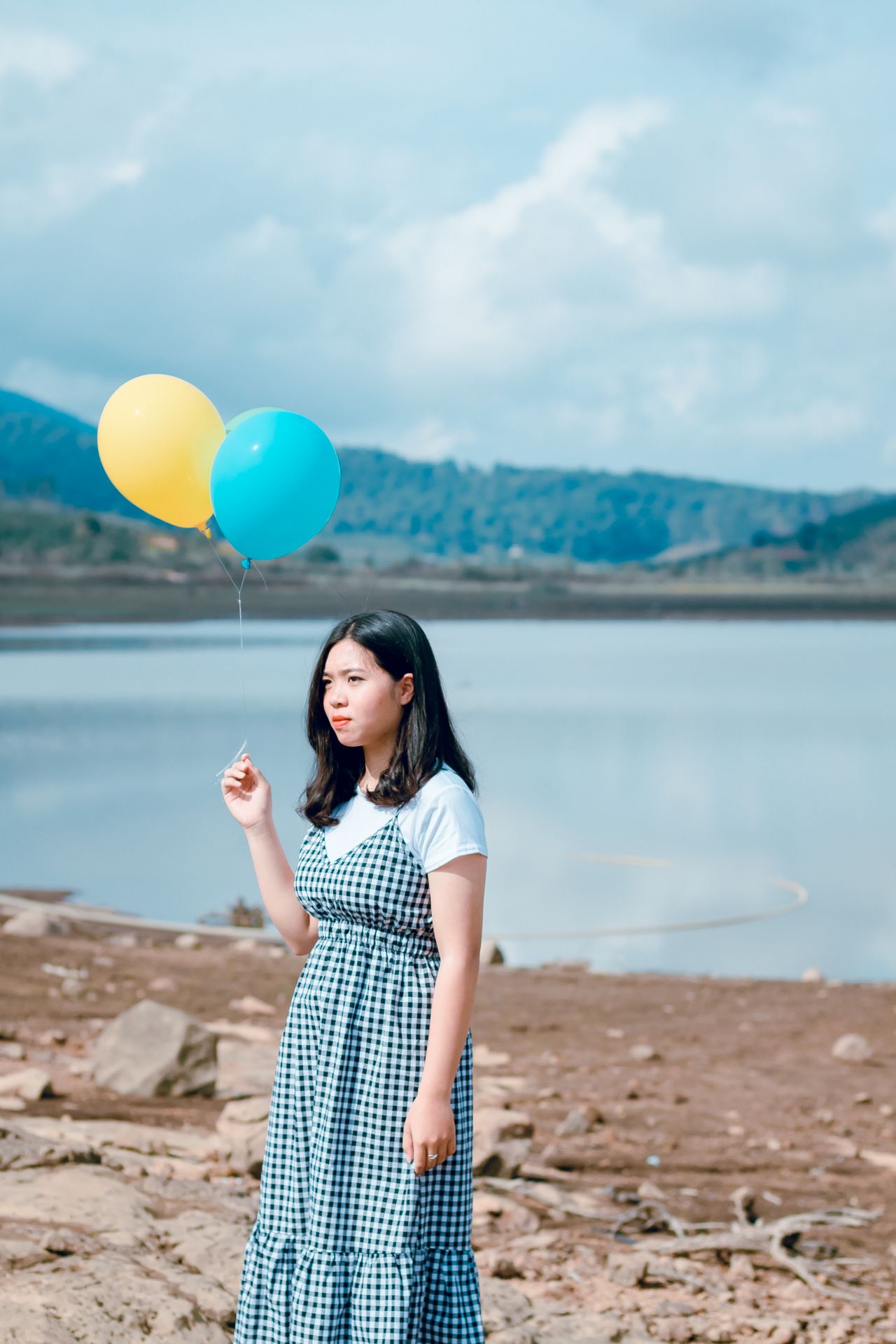 Woman in a gingham dress and white t-shirt holding balloons