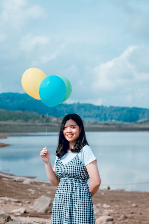 Shallow Focus Photography of Woman in White and Black Short-sleeved Dress Holding Balloons