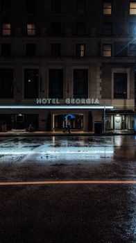 A rainy evening scene at Hotel Georgia in Vancouver, featuring a person walking with an umbrella.