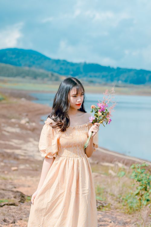 Free A young woman enjoys a sunny day at the lakeside, dressed in a summer gown. Stock Photo