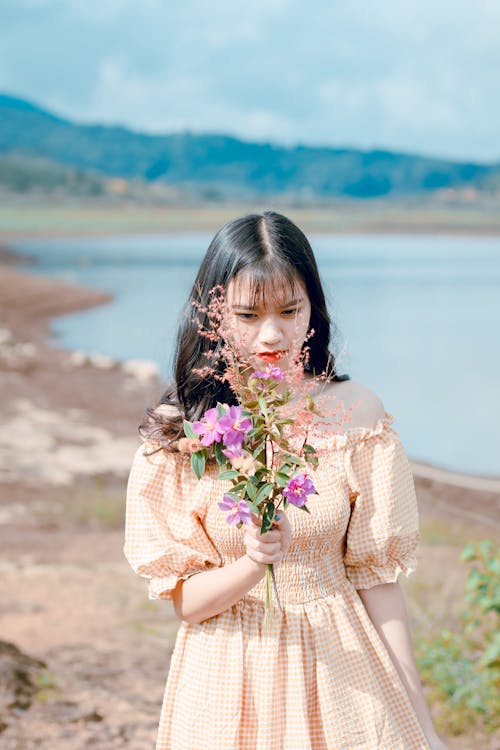 Woman in Orange and White Gingham Check Off-shoulder Dress Holding Pink Petaled Flowers