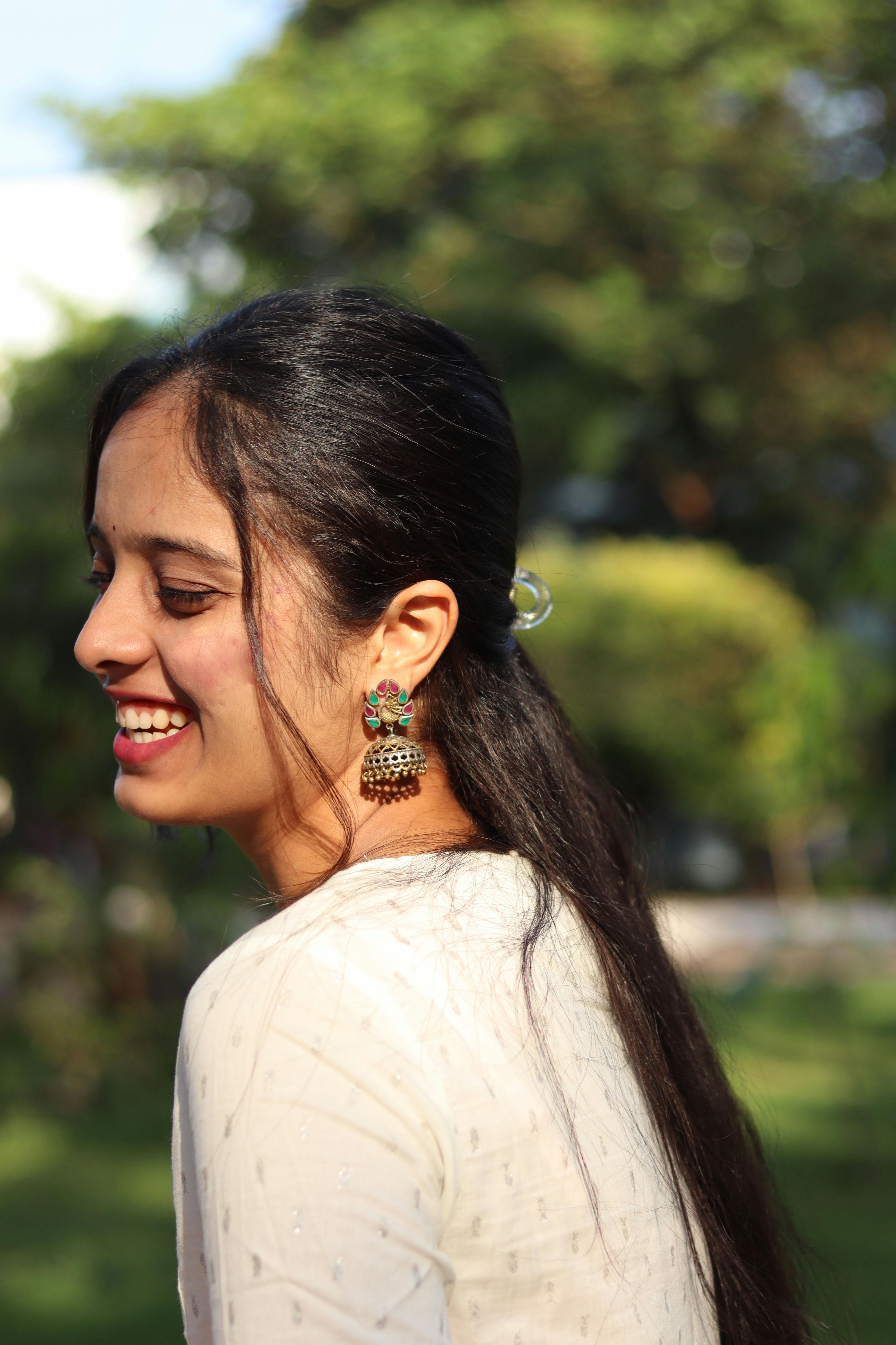 Profile of a young South Asian woman smiling in a sunny park setting.