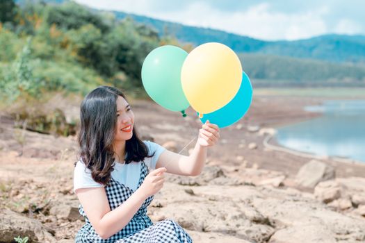 一个快乐的年轻女子在湖边享受阳光明媚的一天，手拿五颜六色的气球