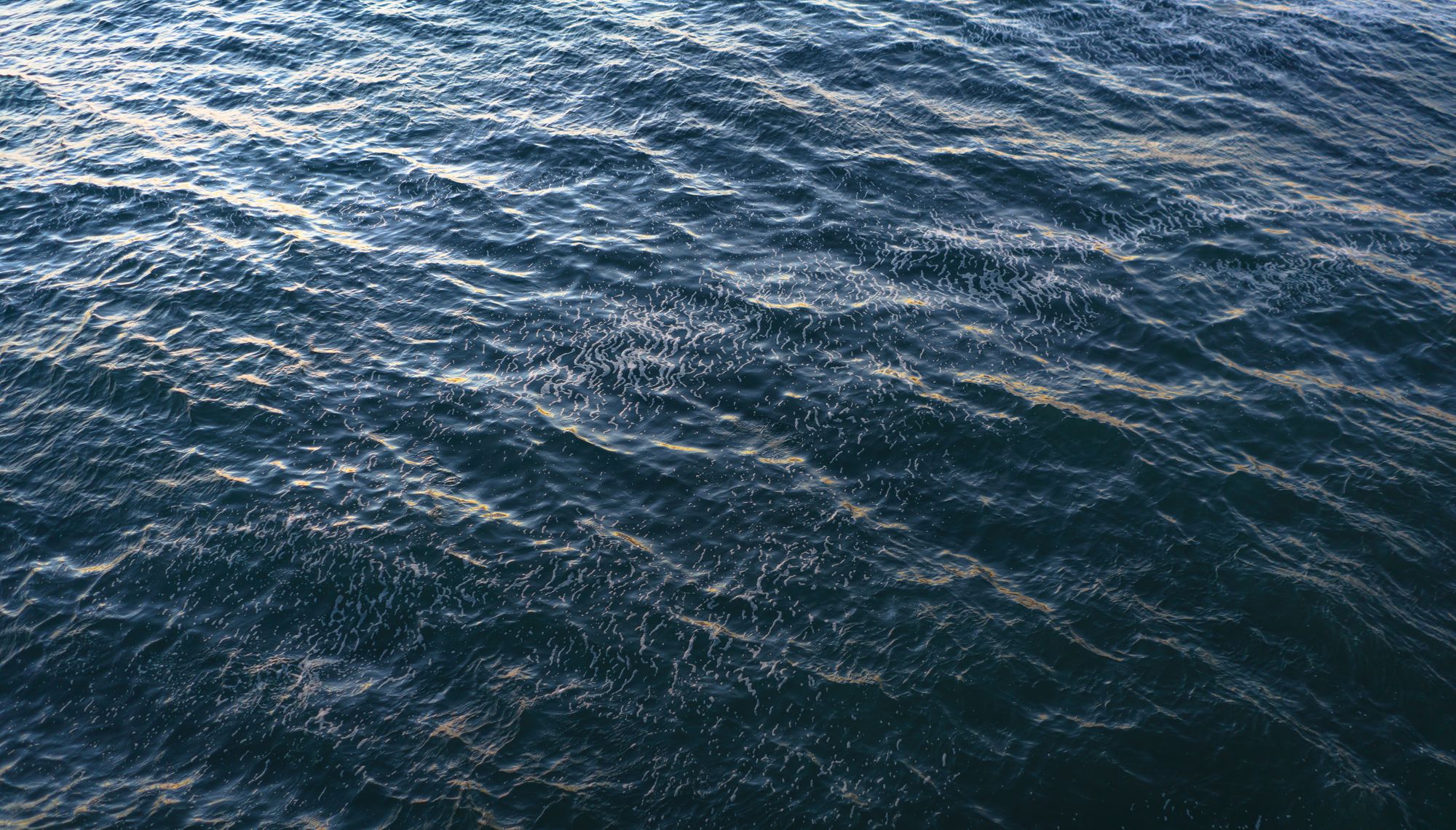A soothing aerial view of ocean waves with ripples and light reflections.