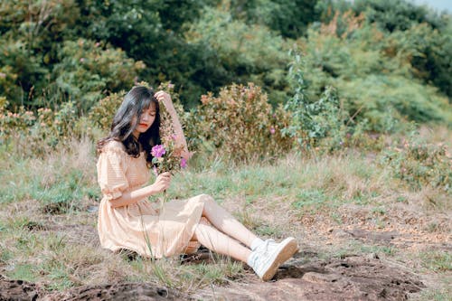 免费 女人穿着棕色的衣服，拿着紫色的花坐在草地上 素材图片