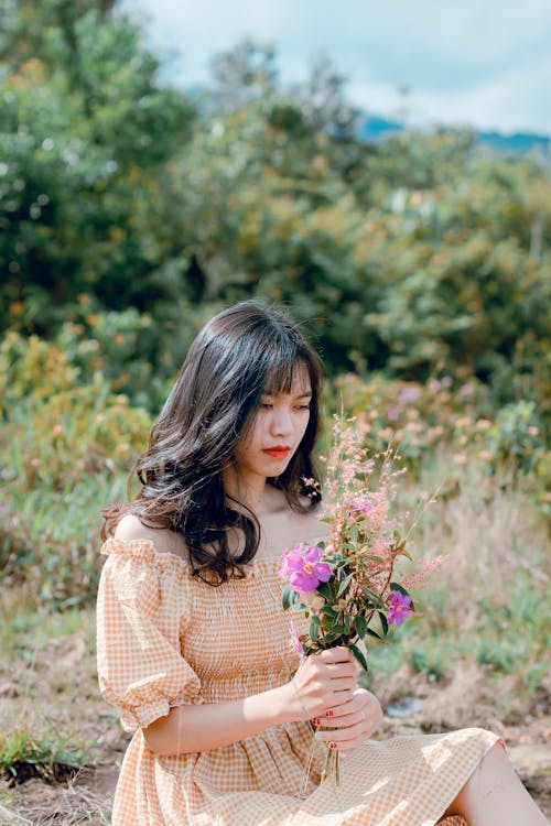 Free Shallow Focus Photography of Woman Wearing Orange Checked Dress Holding Purple Flowers Stock Photo