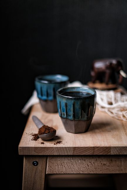 Two ceramic coffee cups on a wooden table with a spoon and a black background.