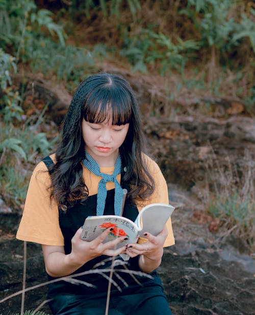 Woman in Orange and Black Top Holding White Book