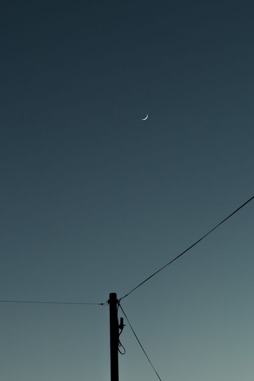 Free A serene evening sky with a crescent moon and silhouetted power lines creating a minimalist composition. Stock Photo