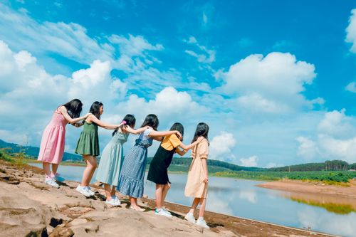 Free Six young women holding hands near a lake, symbolizing friendship and unity. Stock Photo