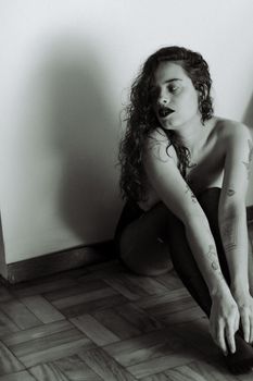 Moody black and white portrait of a woman sitting on the wooden floor indoors.