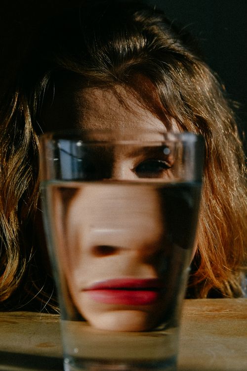 Free Artistic portrait featuring a woman's face distorted by a glass of water in natural light. Stock Photo